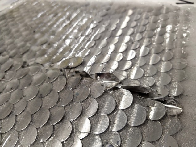 Image with metal plates, placed in the form of scales of fish, after penetration test with visible break between two parts and some coating for stabilisation