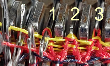 Machine needles from weft knitting machine, with red and yellow yarns building loops in a special way